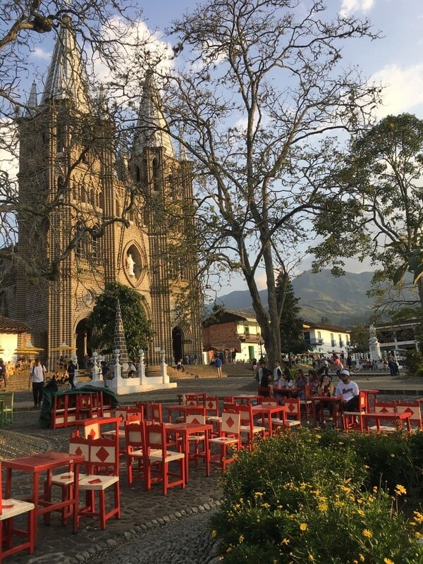 Main square with church, trees, tables and chairs in Colombian colonial town.