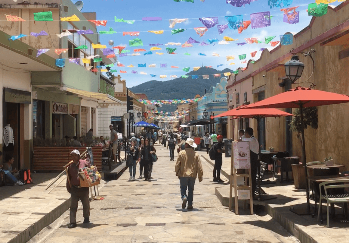 Local people walking during day on the main street in Mexican town, San Cristobal, with buntings hanging on top.
