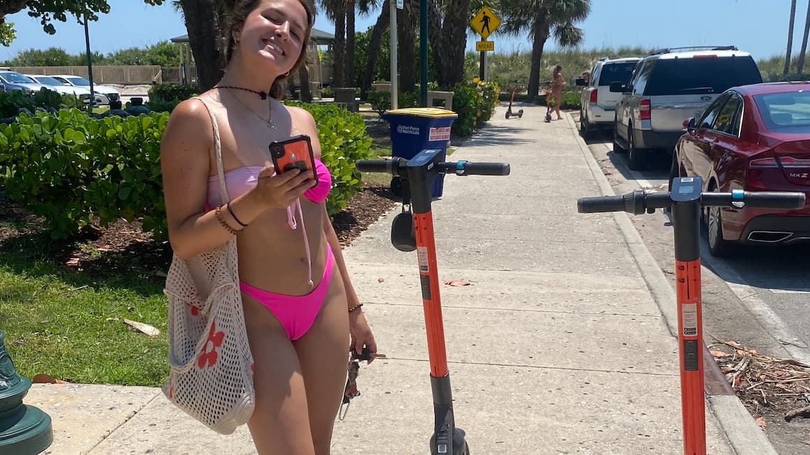 a girl in her bathing suit Smiling in front of two electric scooters at the beach in ,Miami, Florida