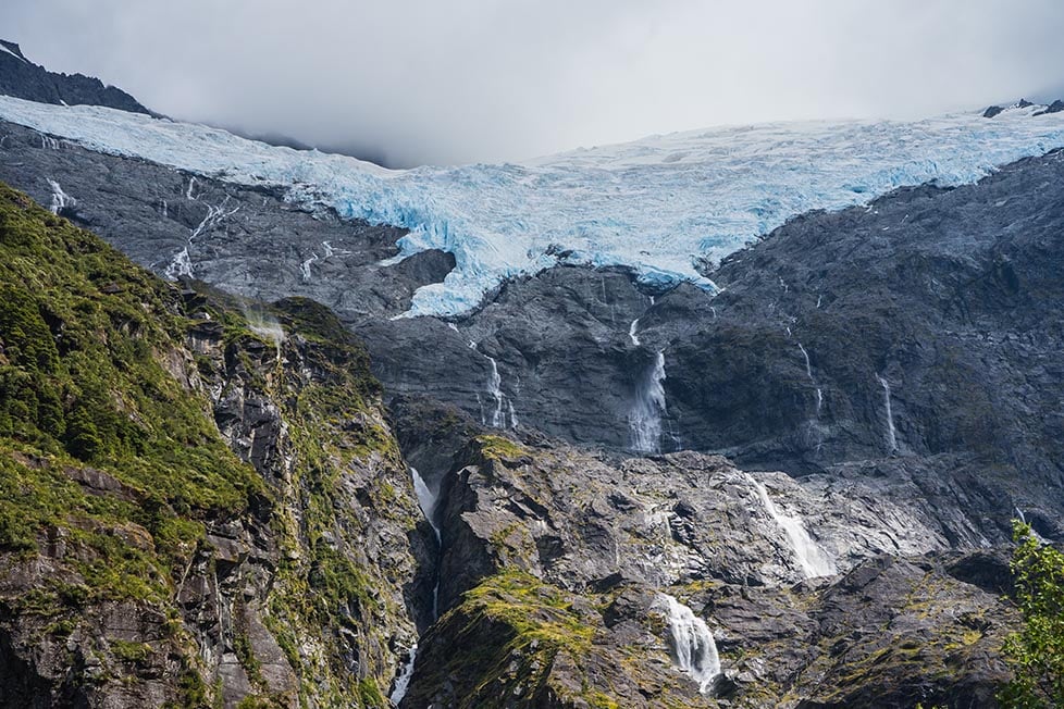 Looking up at a glacier on the top of a mountain with waterfalls coming down near Queenstown, New Zealand.