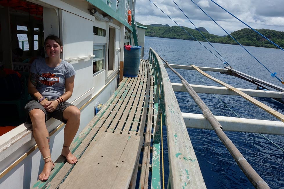 A person sitting on a wooden boat with blue sea and jungle covered islands in the distance.