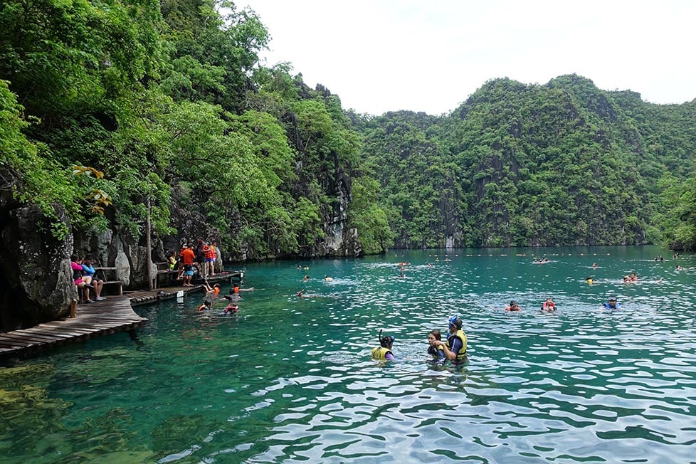 A limestone peak covered in jungle juts out of clear green-blue sea water in Coron, Philippines.