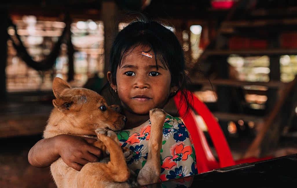 A young girl in a traditional stilt house in Cambodia holding a puppy. Southeast Asia.