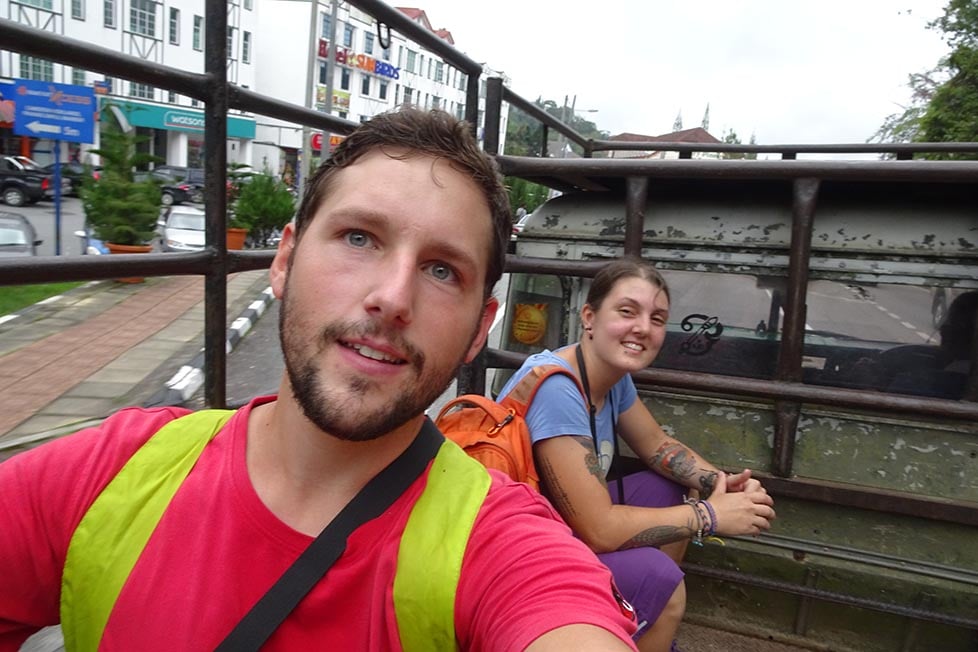 Two people hitchhiking in the back of a pick up truck in Southeast Asia.