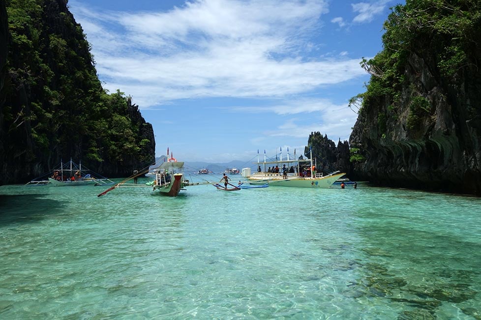 Looking down a shallow inlet surrounded by jungle covered limestone cliffs with clear turquoise sea water and blue skies in the Philippines.