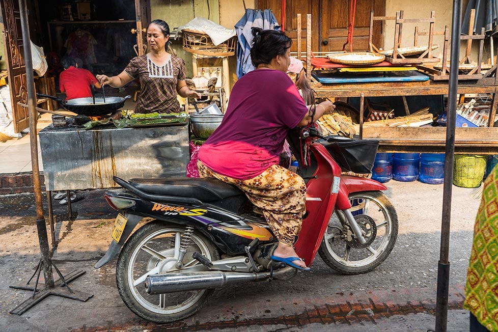 A woman on a motorbike pulling up to buy some street food in Laos, Southeast Asia.