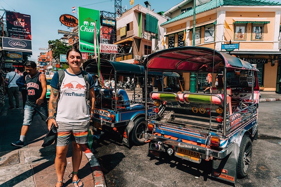 A person standing on Khao San Road in Bangkok, Thailand next to some classic Thai tuk tuks of all colours.