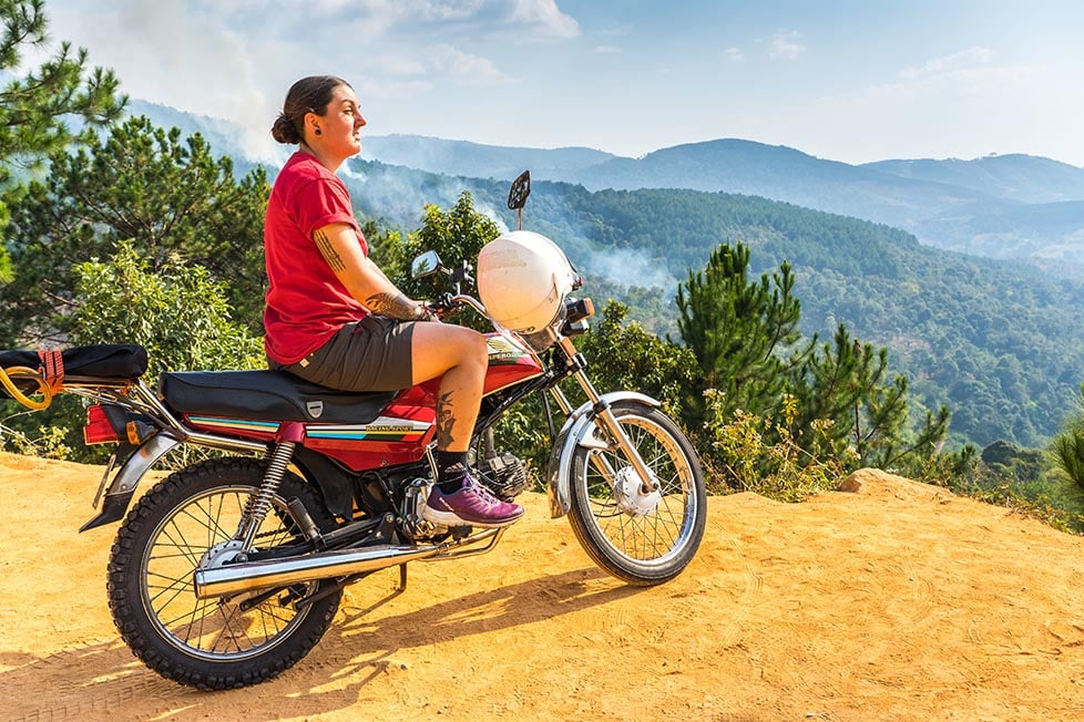 A person sitting on a motorbike looking out over the jungle covered mountains of Vietnam.