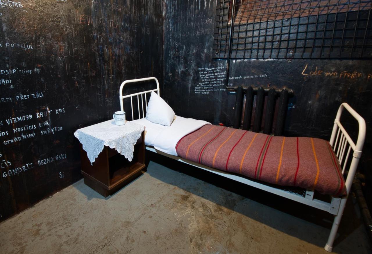 a prison hotel room with a while bed against black walls adorned with steel fixtures.