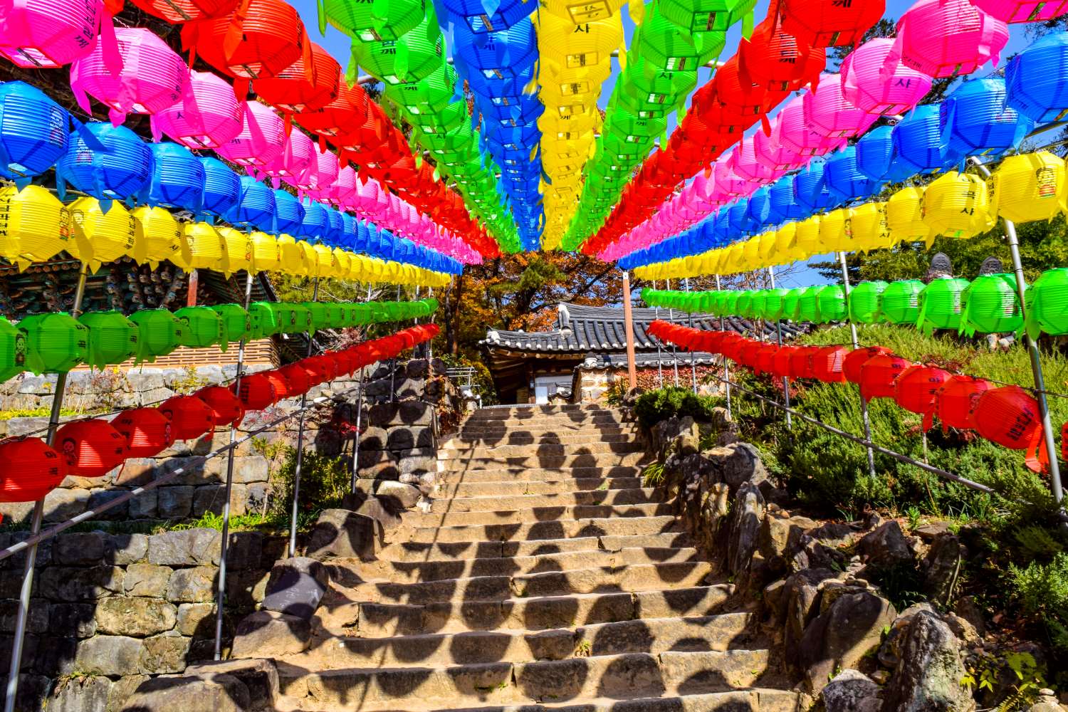 rainbow colored lanterns made into a tunnel going up a stone staircase to a historical building in south korea