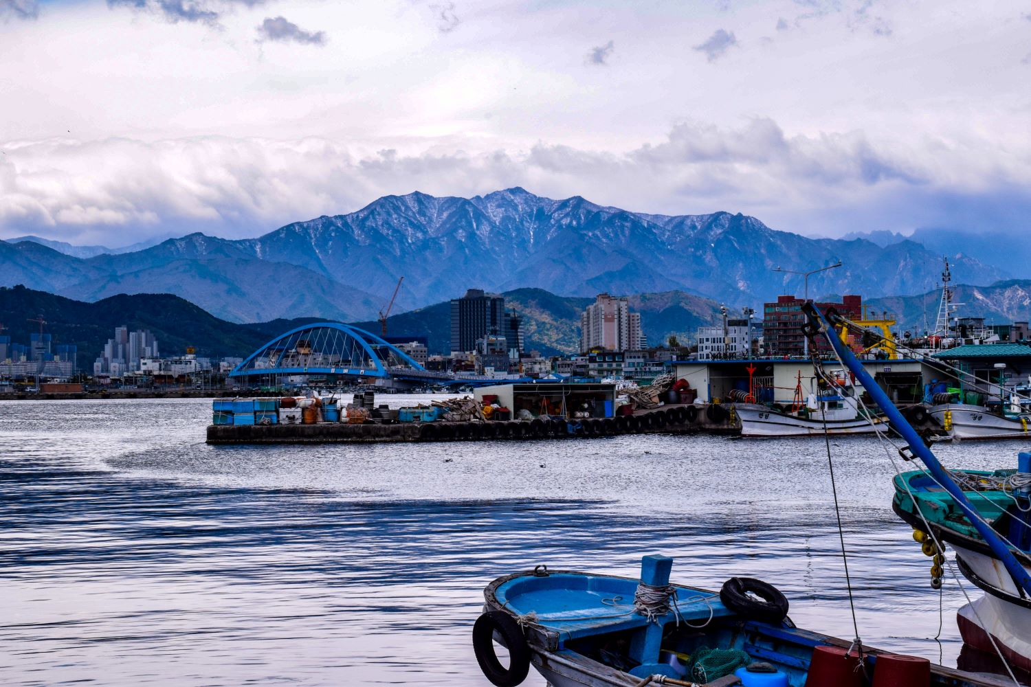 a view of boats on the water and mountains behind them at a port in south korea