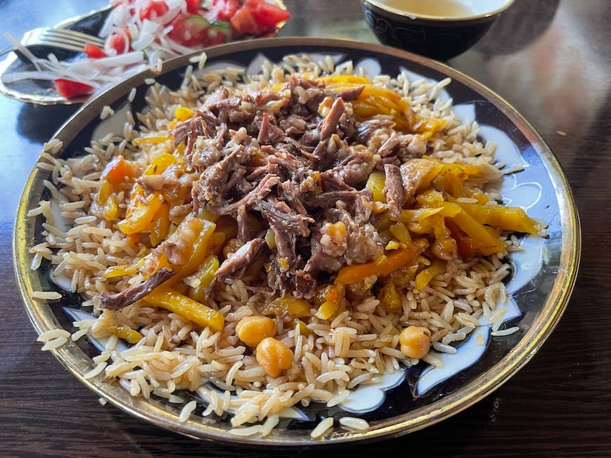 plov sitting on a colored dish with rice vegeatables and braised meat