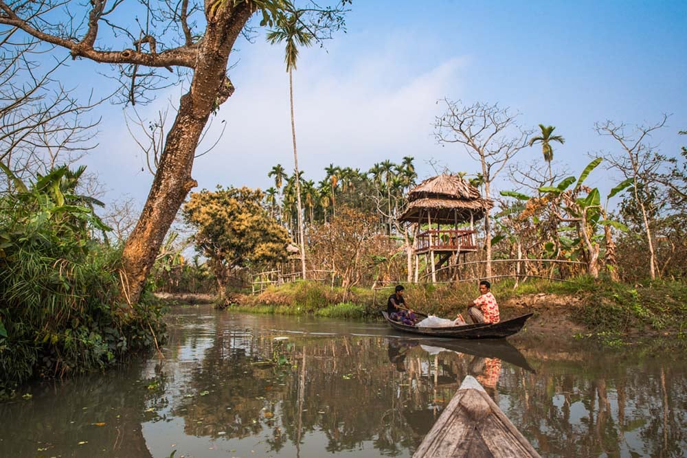locals paddling on a wooden boat on a canal channel in bangladesh
