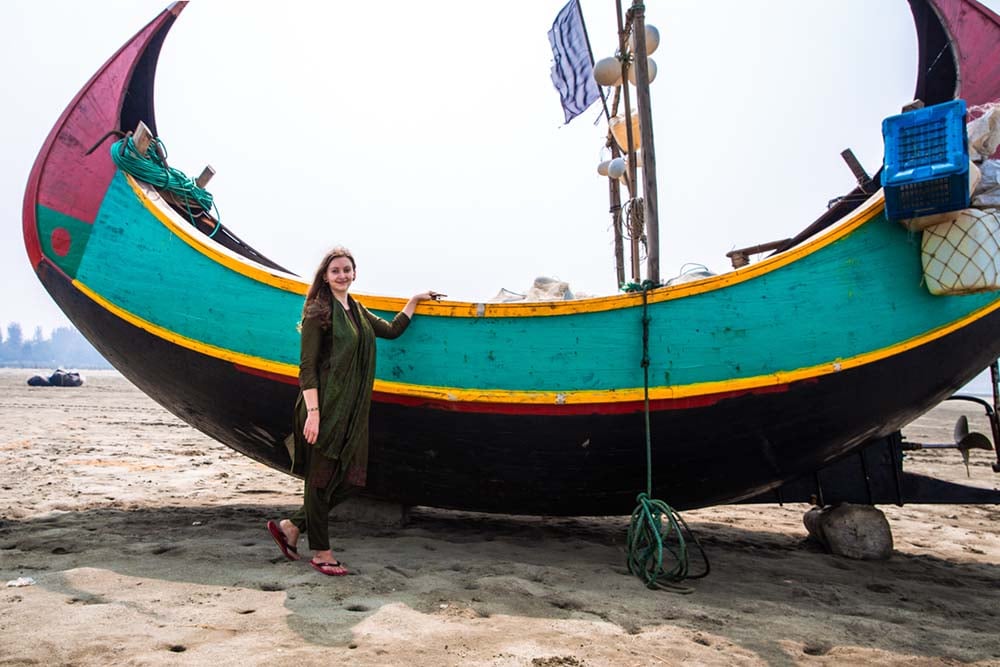a girl standing in front of a wooden boat on a beach in bangladesh