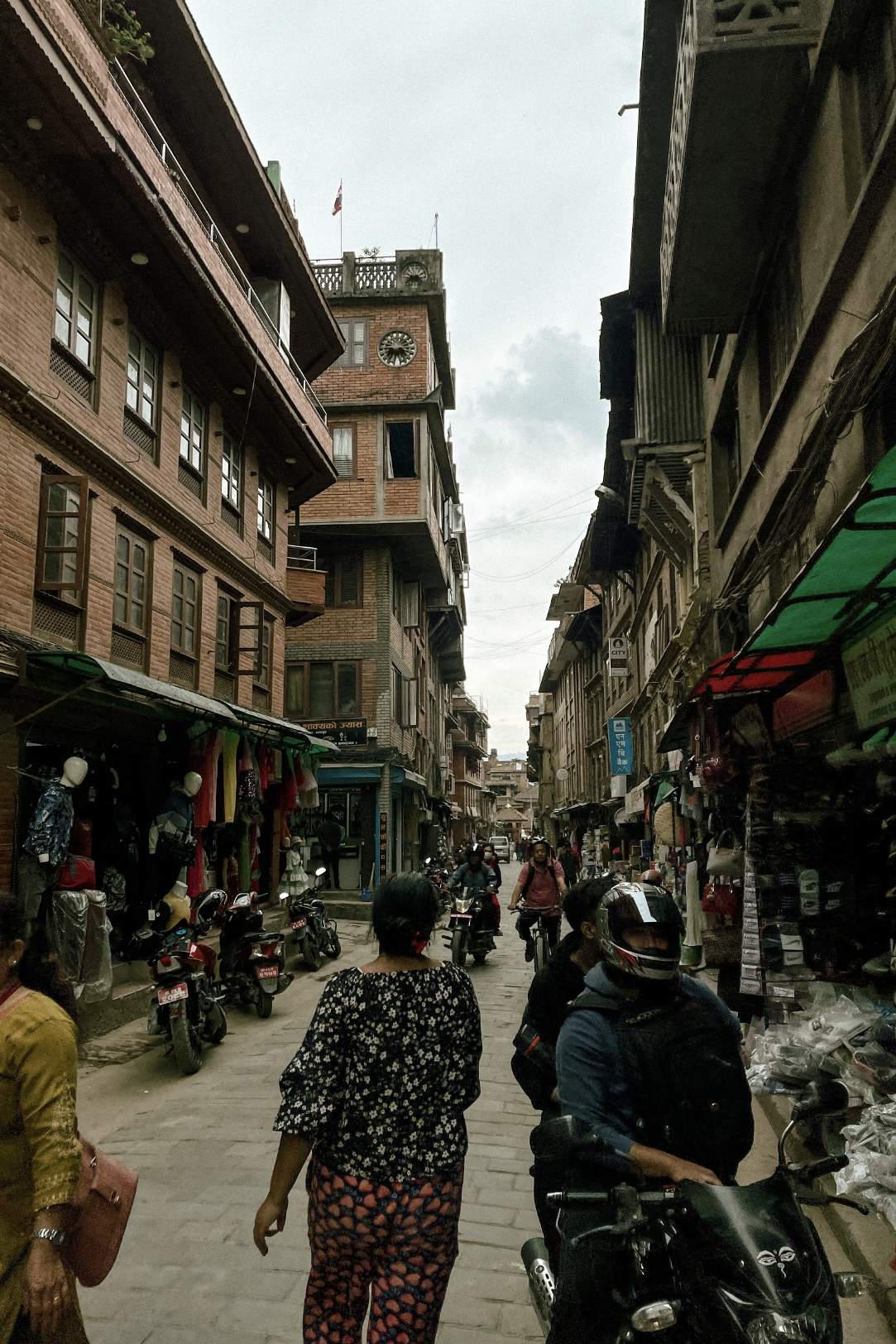 a street scene in kathmandu nepal where locals are walking and motorbiking on the cobblestone pathway