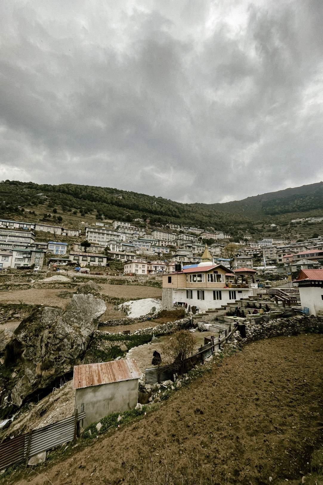 a village in the hills of nepal filled with flat roofed homes in rectangular shapes and taller homes with more triangle like roofs