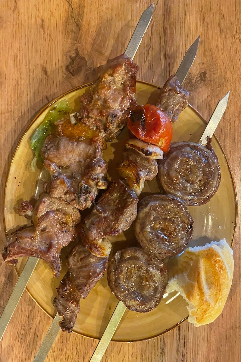 three skewers of kebabs on a plate with bread