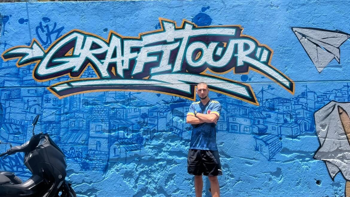 Joe stood in front of a blue Graffiti tour wall in Comuna 13, Medellin, Colombia