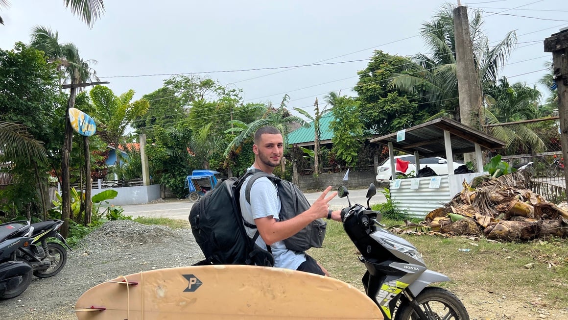 Joe on a scooter with a surfboard and Osprey Farpoint 40 - Hand lugagge only