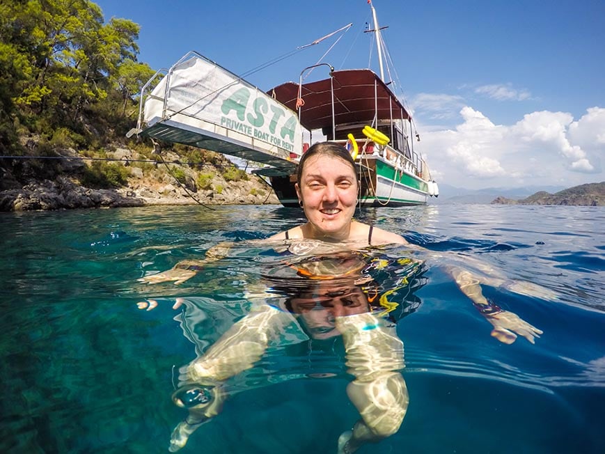 Nic swimming in the sea off the coast of Turkey in clear blue water with a boat behind them.