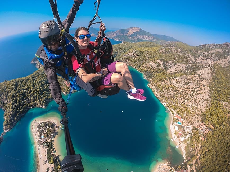 Nic paragliding over the blue lagoon in Oludeniz near Fethiye in Turkey shot on a GoPro. Below them is a mountainous landscape and beautiful blue ocean.