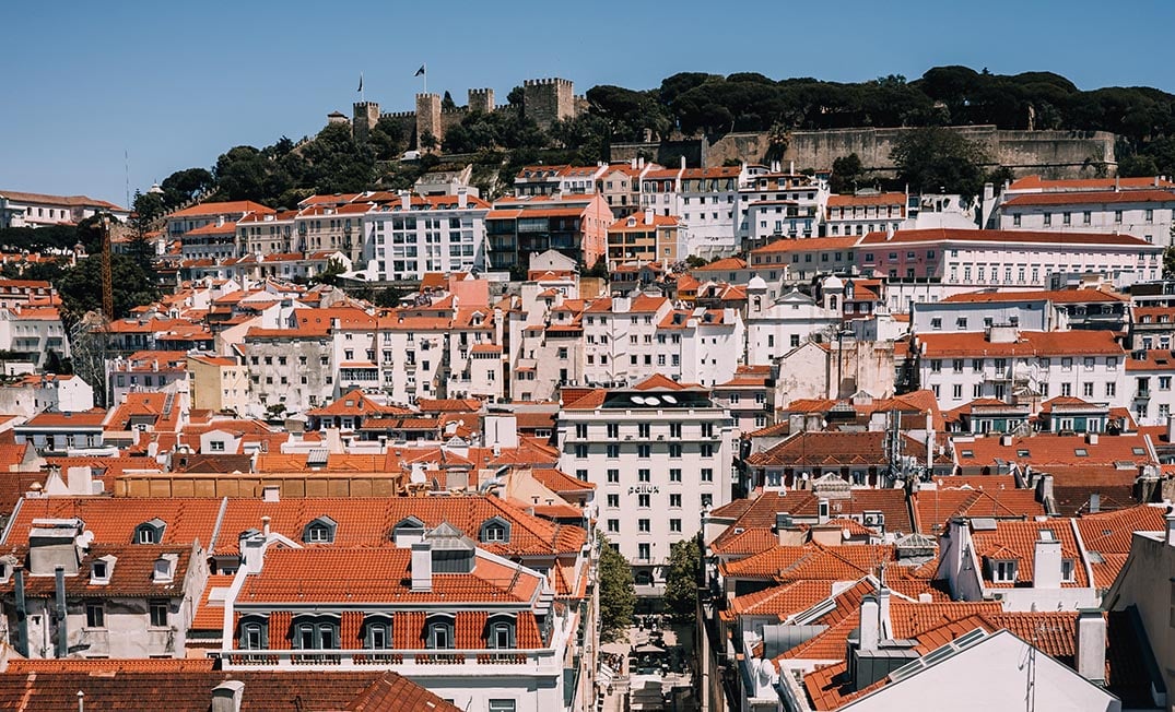 The view over Lisbon, Portugal with the castle beyond many orange terracotta rooftops.