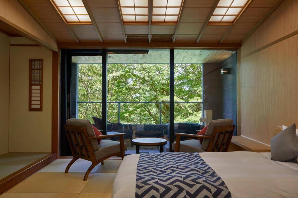 A bedroom in a traditional Japanese ryokan with queen bed, and a seating area with a breathtaking view of nature