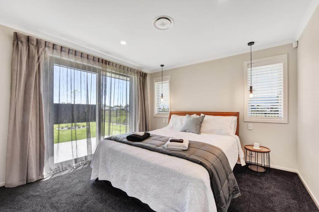 Bedroom with a king-size bed with a white comforter and a sliding glass door leading to a balcony