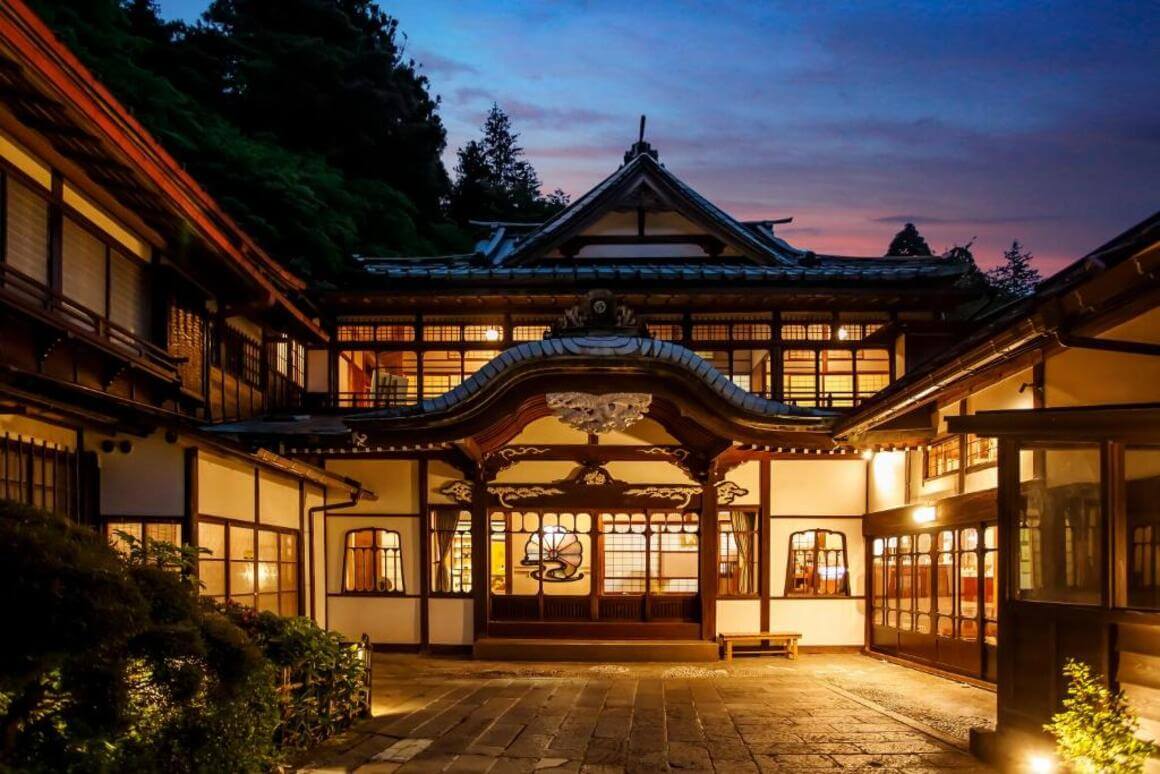 Main entrance of Kowakien Mikawaya Ryokan, softly illuminated by yellow lighting and adorned with traditional Japanese architectural design
