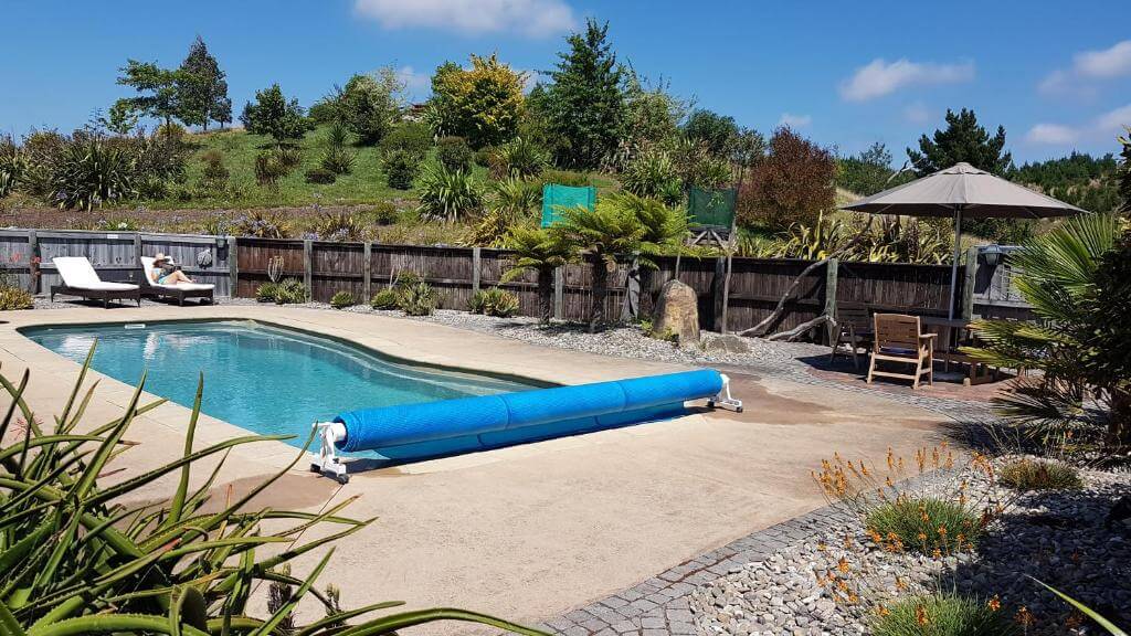 A blue swimming pool with a blue cover on it in a backyard surrounded by a wooden fence.