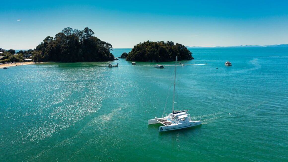 A Catamaran cruising in the ocean just a few metres from the beach from a birds eye view.