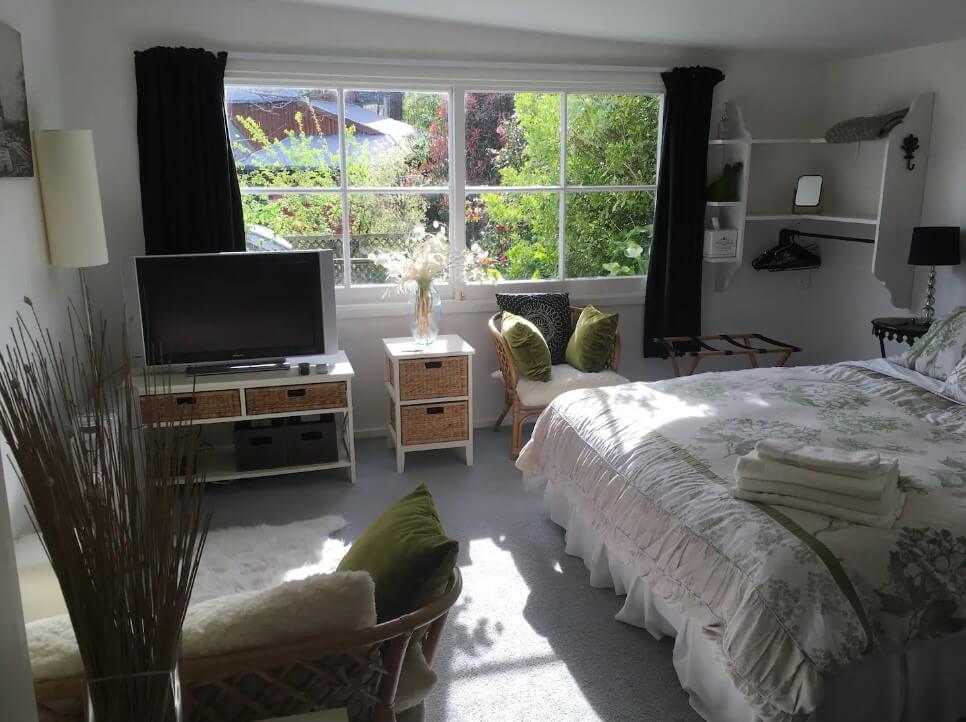 Sunny room with a king-size bed, white furniture, and a big window in Richmond, New Zealand.