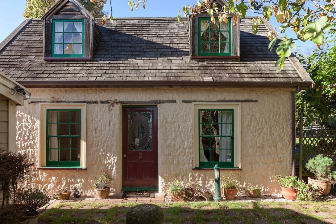 Exterior of a small, rustic cottage with a red door and green windows in Richmond, New Zealand