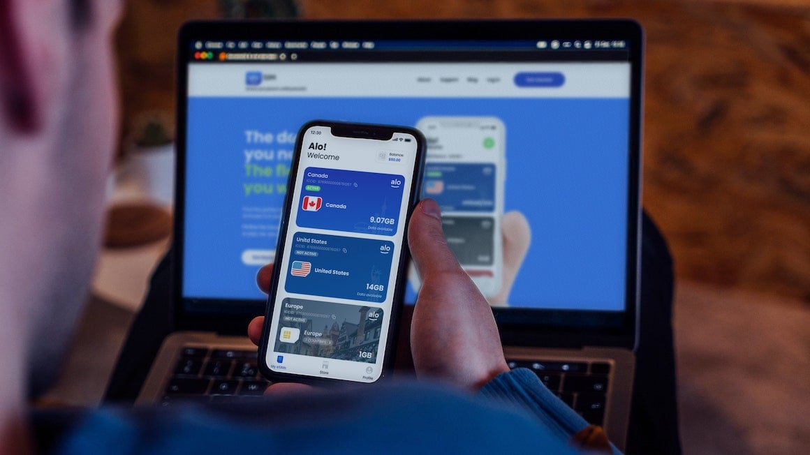 person holding a phone with the aloSIM app open with the website open on their laptop