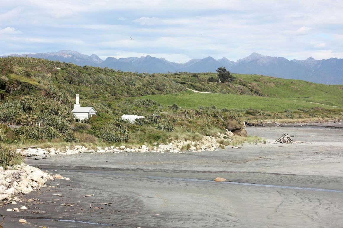 A house sits on a hill overlooking a beach with mountains in the background in Cape Foulwind