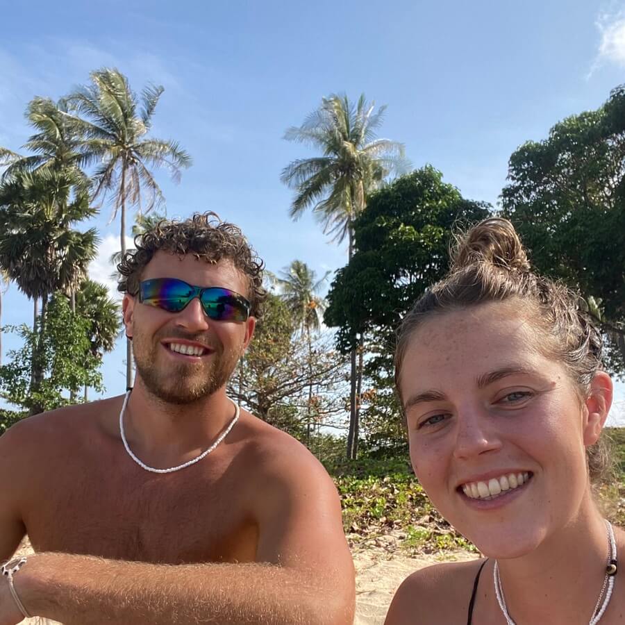 Harv and Dani smiling at the beach with palm trees behind them