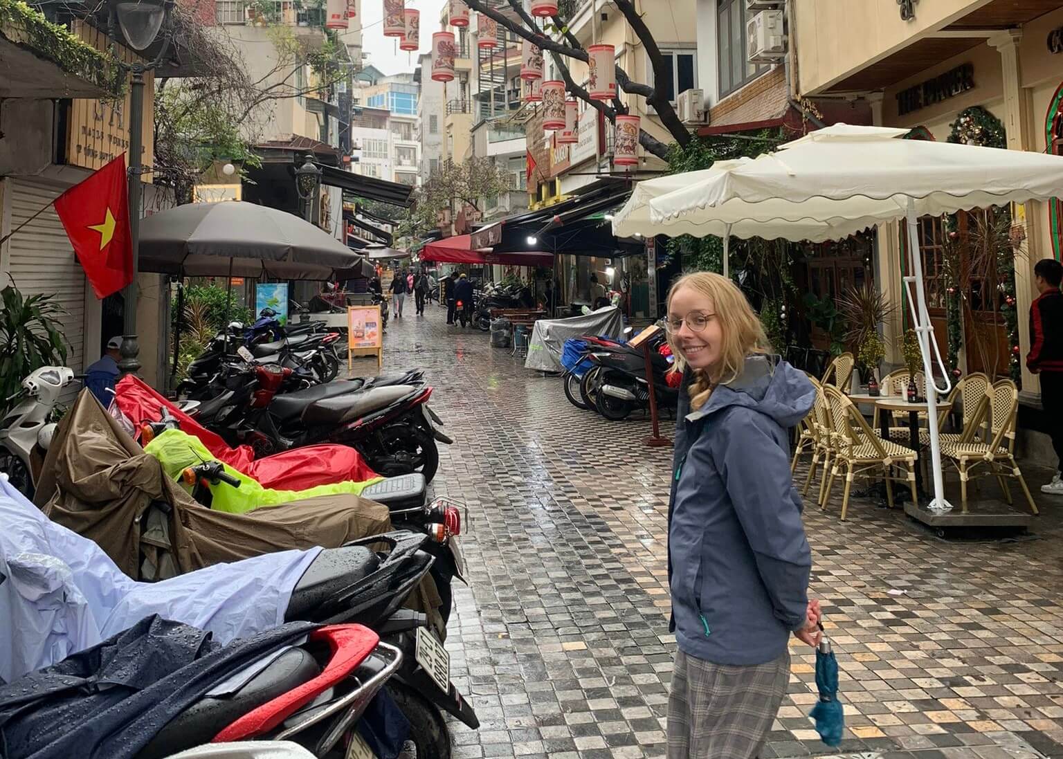 Laura smiling painfully in the wet steets of hanoi in front of motorbikes and restaurants