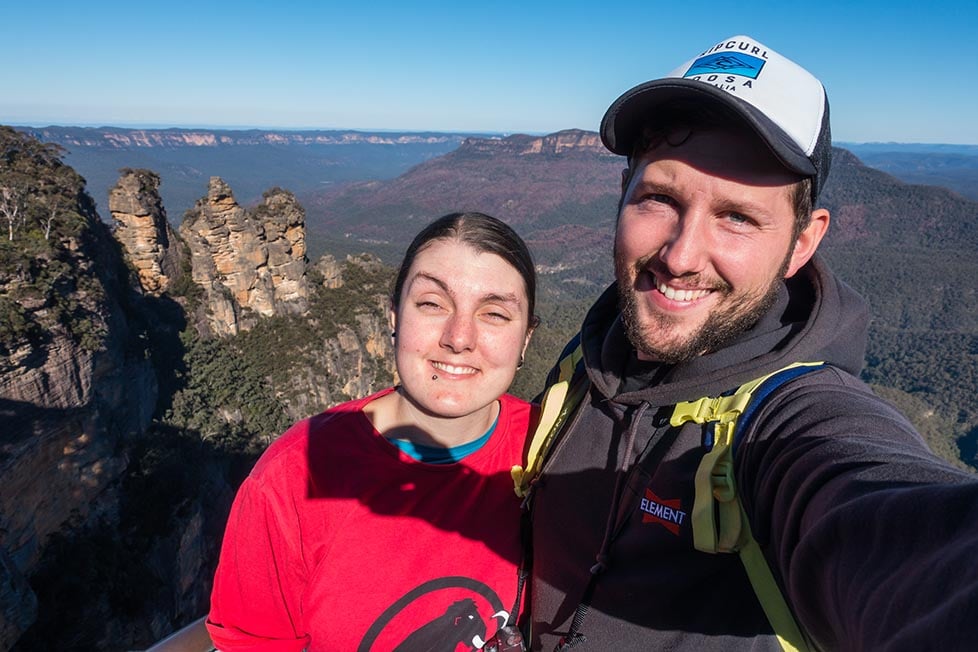 Nic and Shorty taking a selfie in the Blue Mountains with the Three Sisters rock formation in the background and behind that a wide visa of a mountain range.