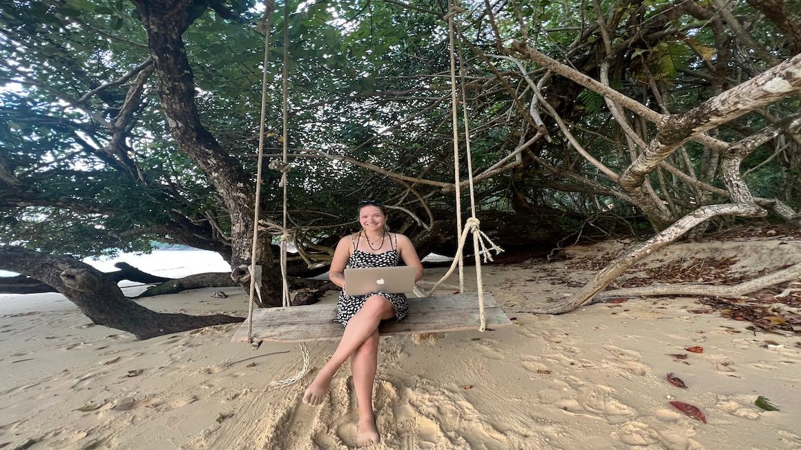 girl sitting on a swing on a beach with a laptop living the digital nomad life