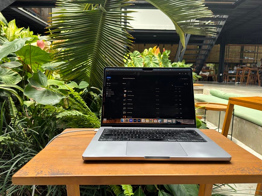 A laptop on a table in a co working hostel with plants next to the table.