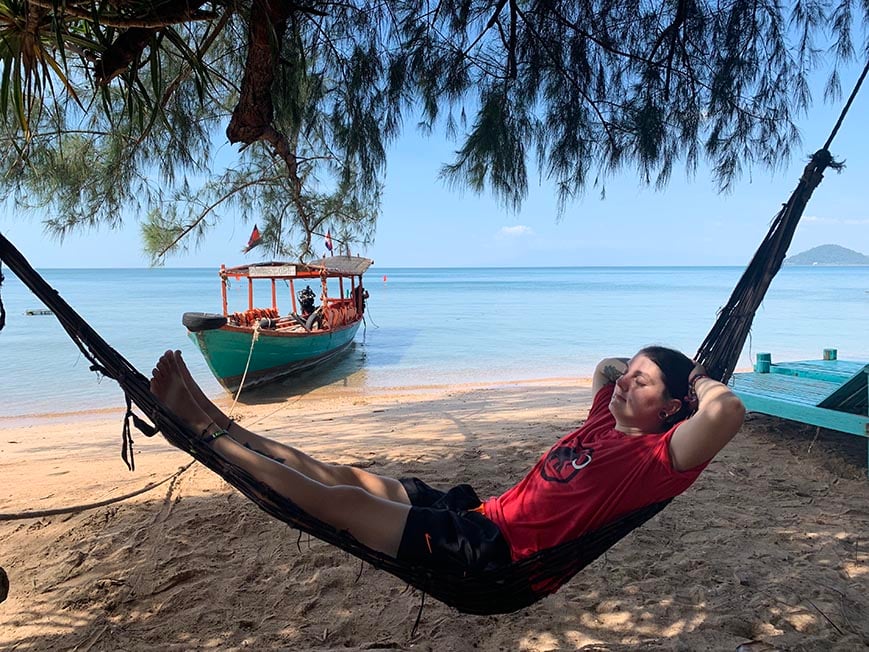 Nic chilling out on a Hammock on a beach with the sea behind them and a boat floating.