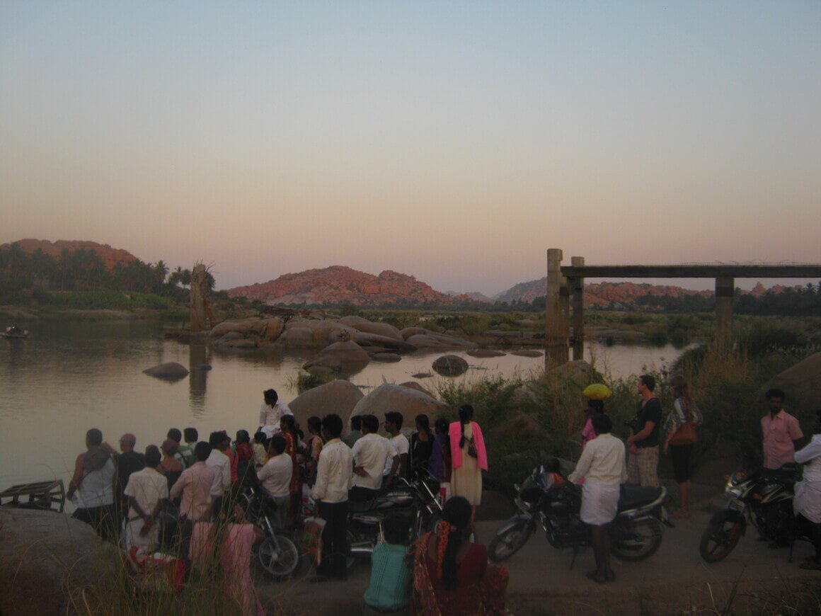 Crowds of people waiting by the side of a river after sunset