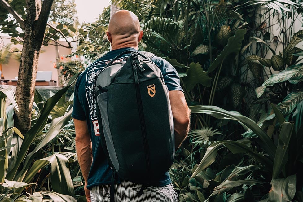 A man walking through a jungle wearing the Nemo Vantage backpack, he is looking away from the camera.