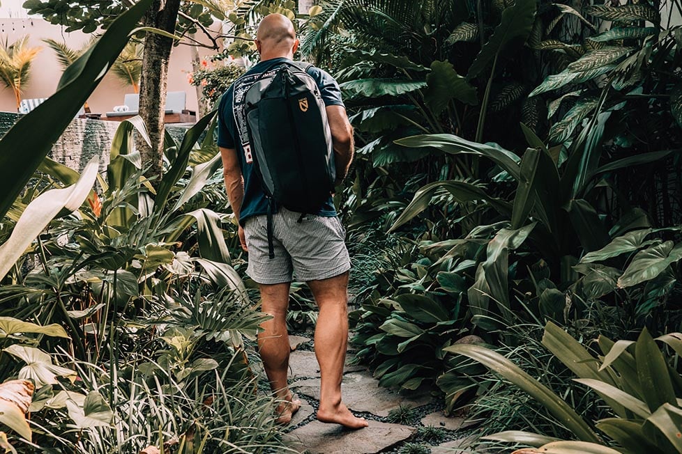 A man walking through a jungle wearing the Nemo Vantage backpack, he is looking away from the camera.