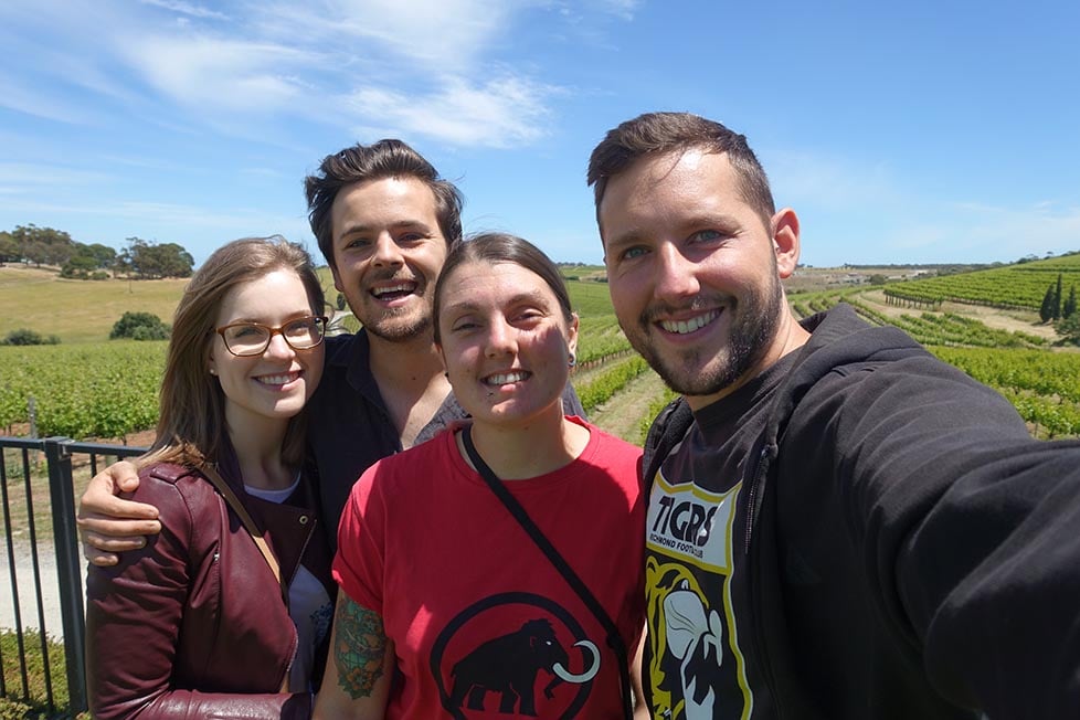 four people smiling in front of a vinyard 