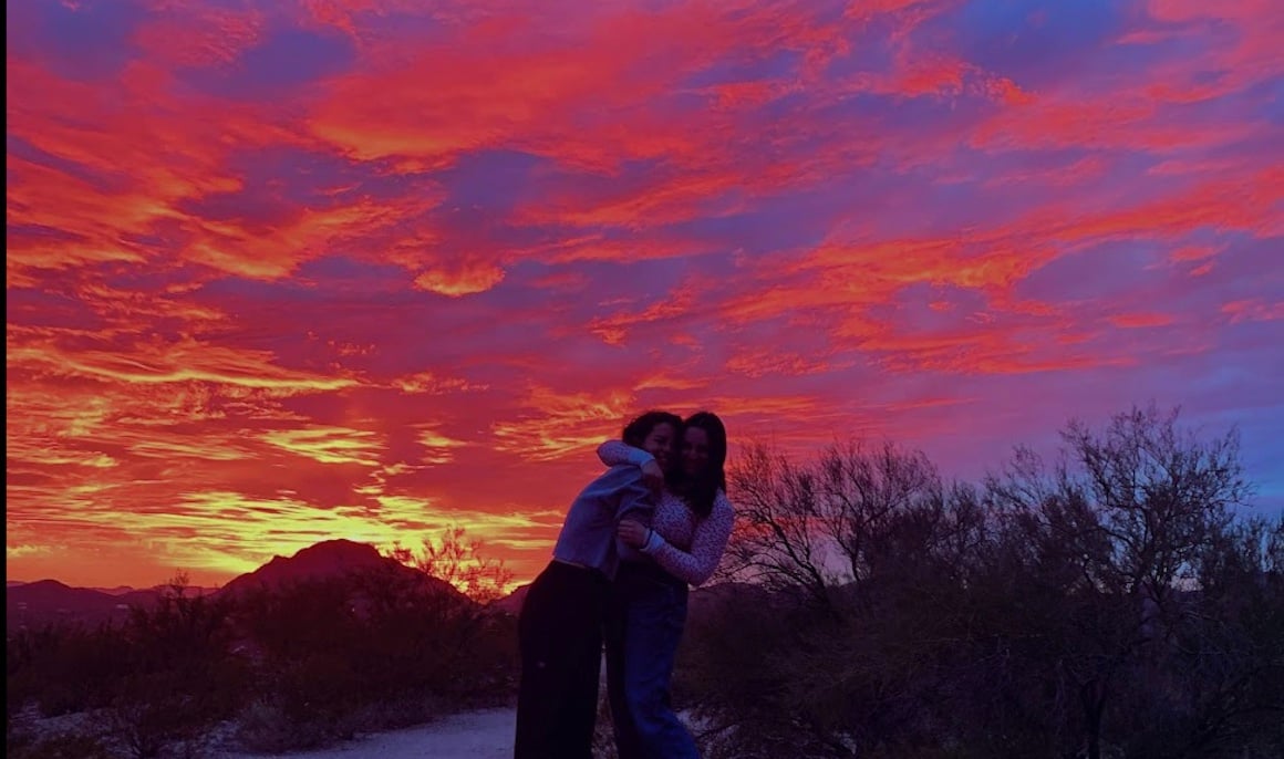 Friends embrace eachother in a hug as a colorful sunset fills the sky of Tucson Arizona.