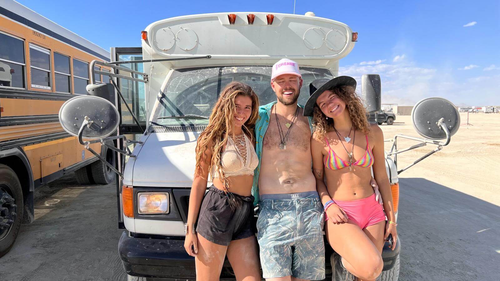 Aud, Amanda, and a kind stranger stood smiling in front of a bus in the desert