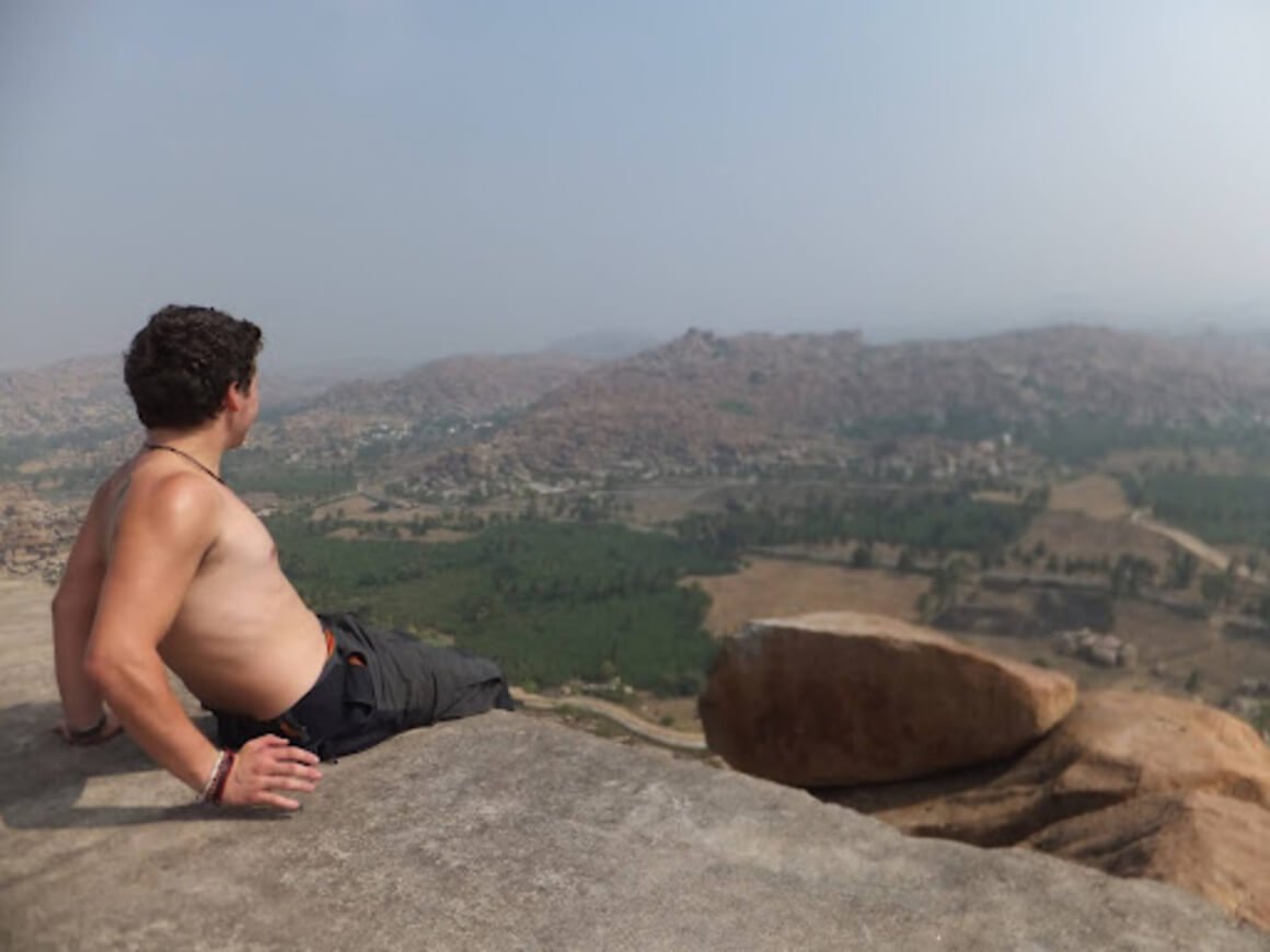 Shirtless will sitting on top of a cliff taking in a breathtaking view of India.