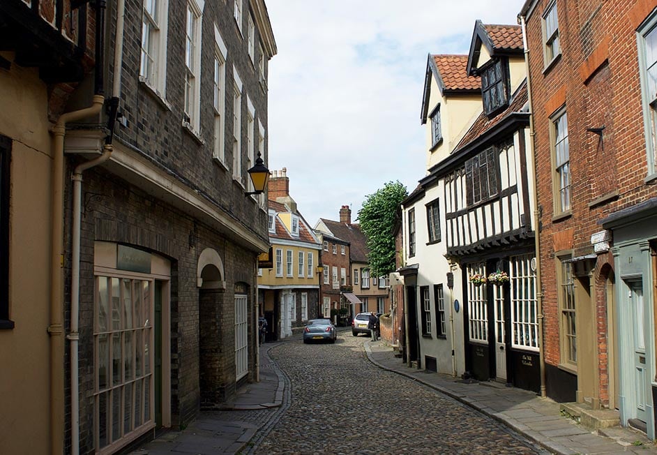Looking down an old cobbled road with wooden and brick Tudor houses in Norwich, England, United Kingdom.