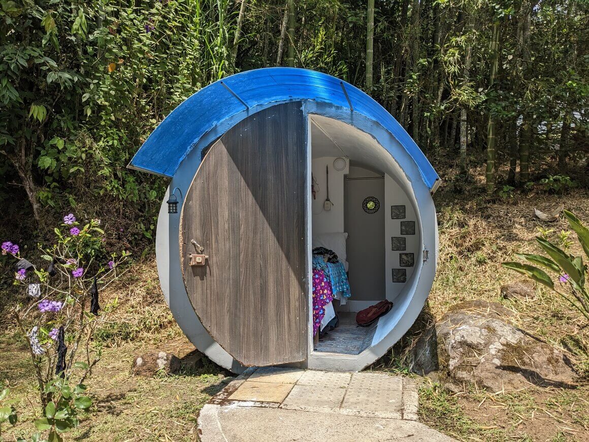Small cylindrical room make of concrete with a semi-circle door with a bed inside in a green natural area